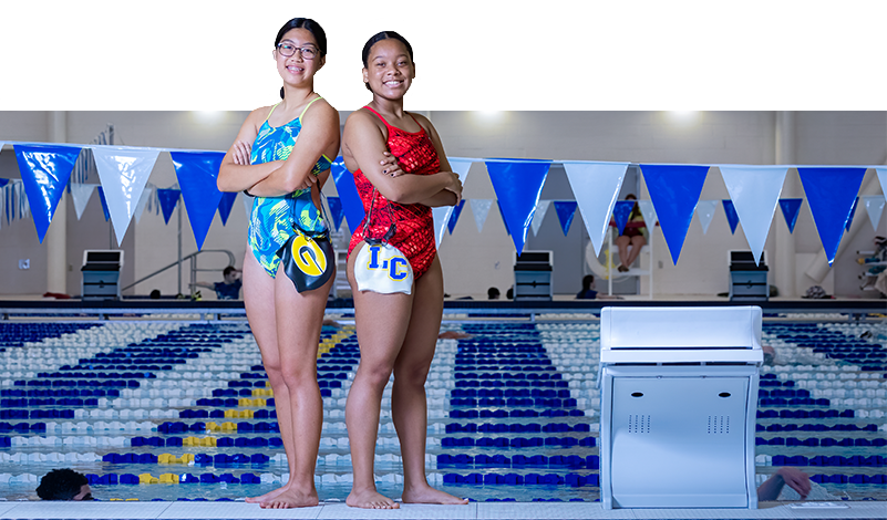 Two HS swimmers posing together in front of the pool