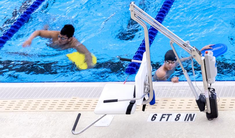 Two students swimming next to the pool lift for wheelchairs