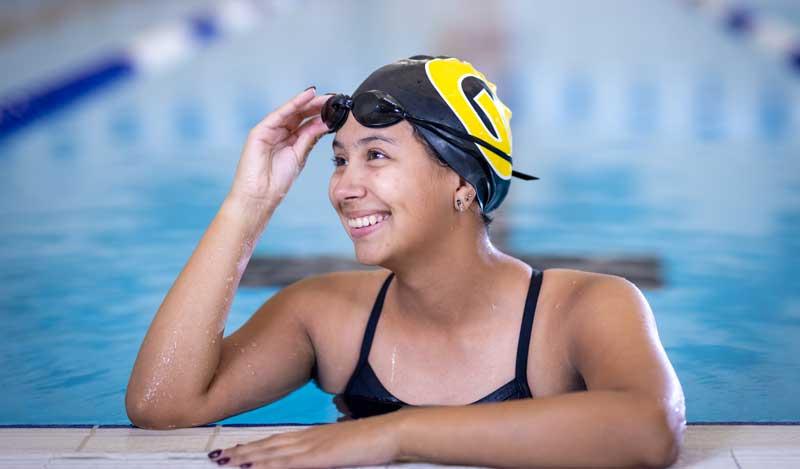 A smiling GHS swimmer adjusting her goggles while holding onto the pool edge